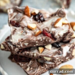 Sweet-Tart Cranberry Almond Chocolate Bark 7 Stacked pieces of Cranberry-Almond Chocolate Bark on a white plate
