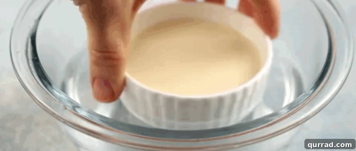 Velvety Vanilla Panna Cotta Treat 8 A ramekin containing panna cotta being dipped into a shallow bowl of hot water to aid in unmolding.