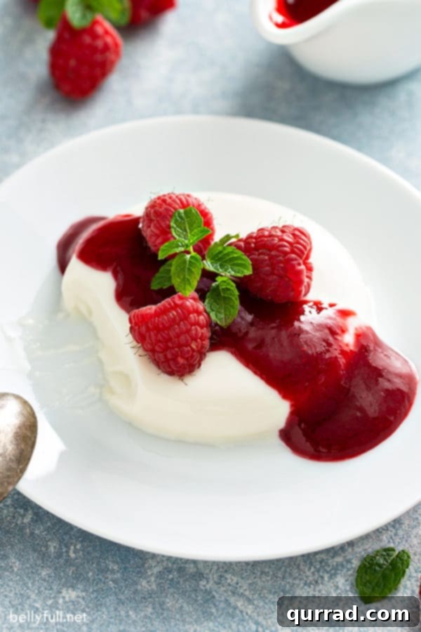 Velvety Vanilla Panna Cotta Treat 10 A beautifully unmolded vanilla panna cotta on a white plate, drizzled with raspberry sauce and garnished with fresh raspberries and mint leaves.