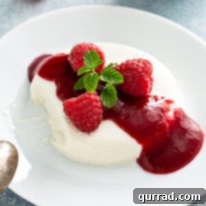 Panna cotta unmolded onto a white plate with raspberry sauce and garnished with fresh mint.