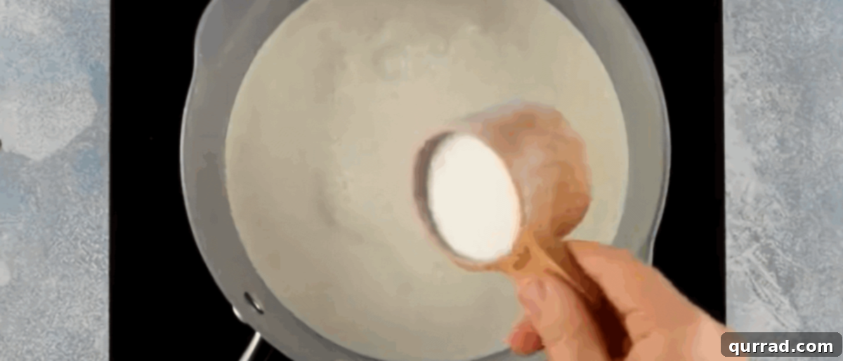 Velvety Vanilla Panna Cotta Treat 5 A saucepan on a stovetop with heavy cream, half and half, and sugar being whisked together over medium heat.