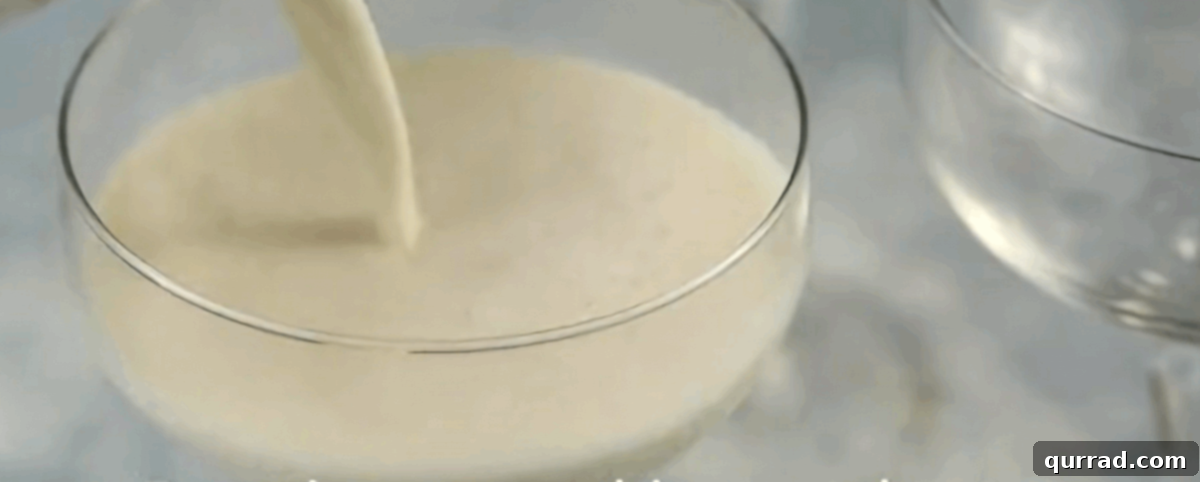 Velvety Vanilla Panna Cotta Treat 7 The smooth panna cotta mixture being poured into individual glass dessert cups set on a tray.