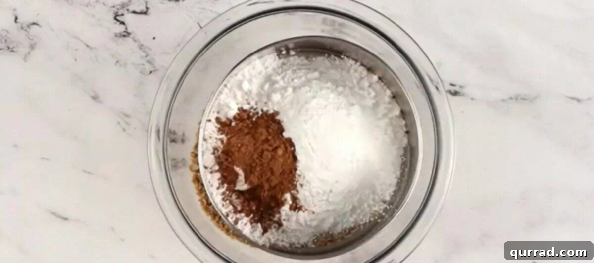 A sifter being used to sift powdered sugar, cocoa powder, and salt over a bowl of cookie and pecan crumbs.