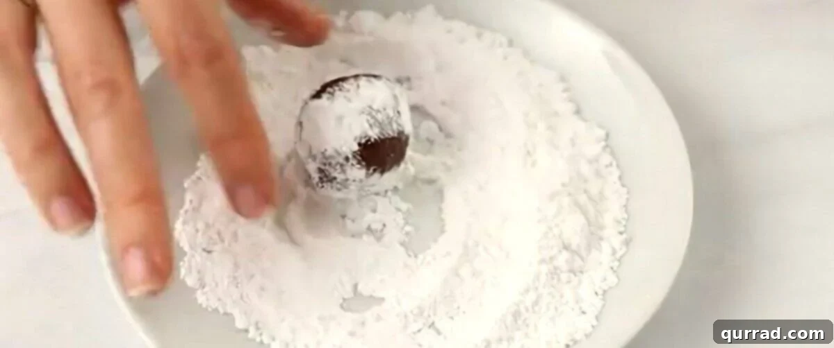 A rum ball being rolled in powdered sugar, creating a beautiful white coating.