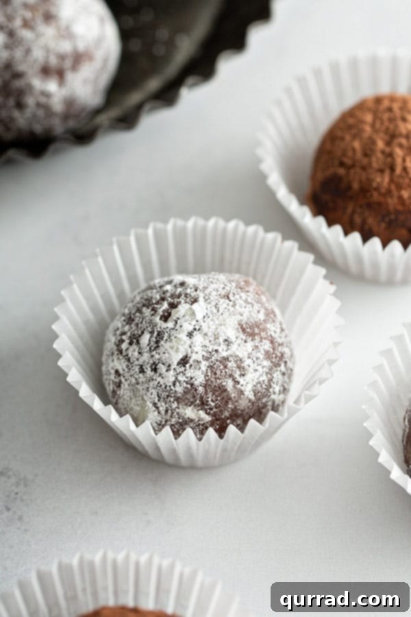 A single rum ball, perfectly coated in powdered sugar, resting in a small paper cup.