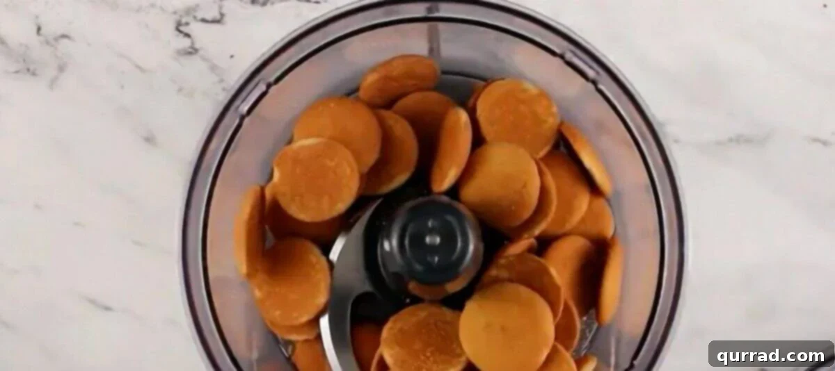 Nilla Wafers being pulsed into fine crumbs inside a food processor bowl.