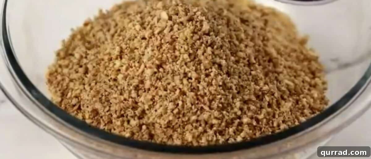 A glass mixing bowl containing both fine cookie crumbs and finely processed pecans, ready for further mixing.