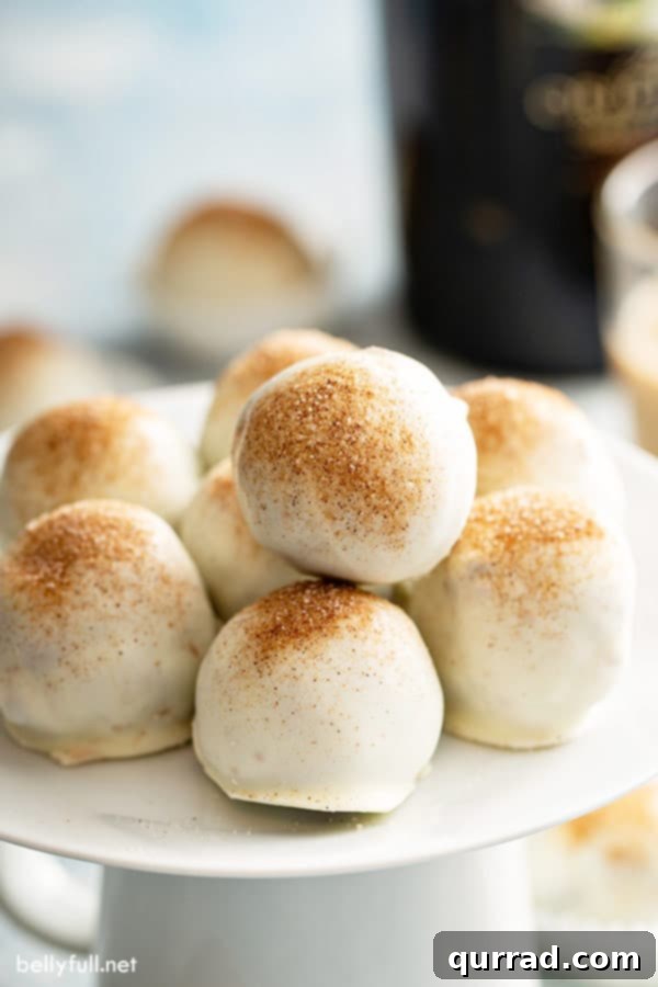 Decadent Bailey's Truffles 3 A collection of perfectly round, white-coated Bailey's Chocolate Truffles, lightly sprinkled with cinnamon-sugar, arranged on an elegant cake stand.