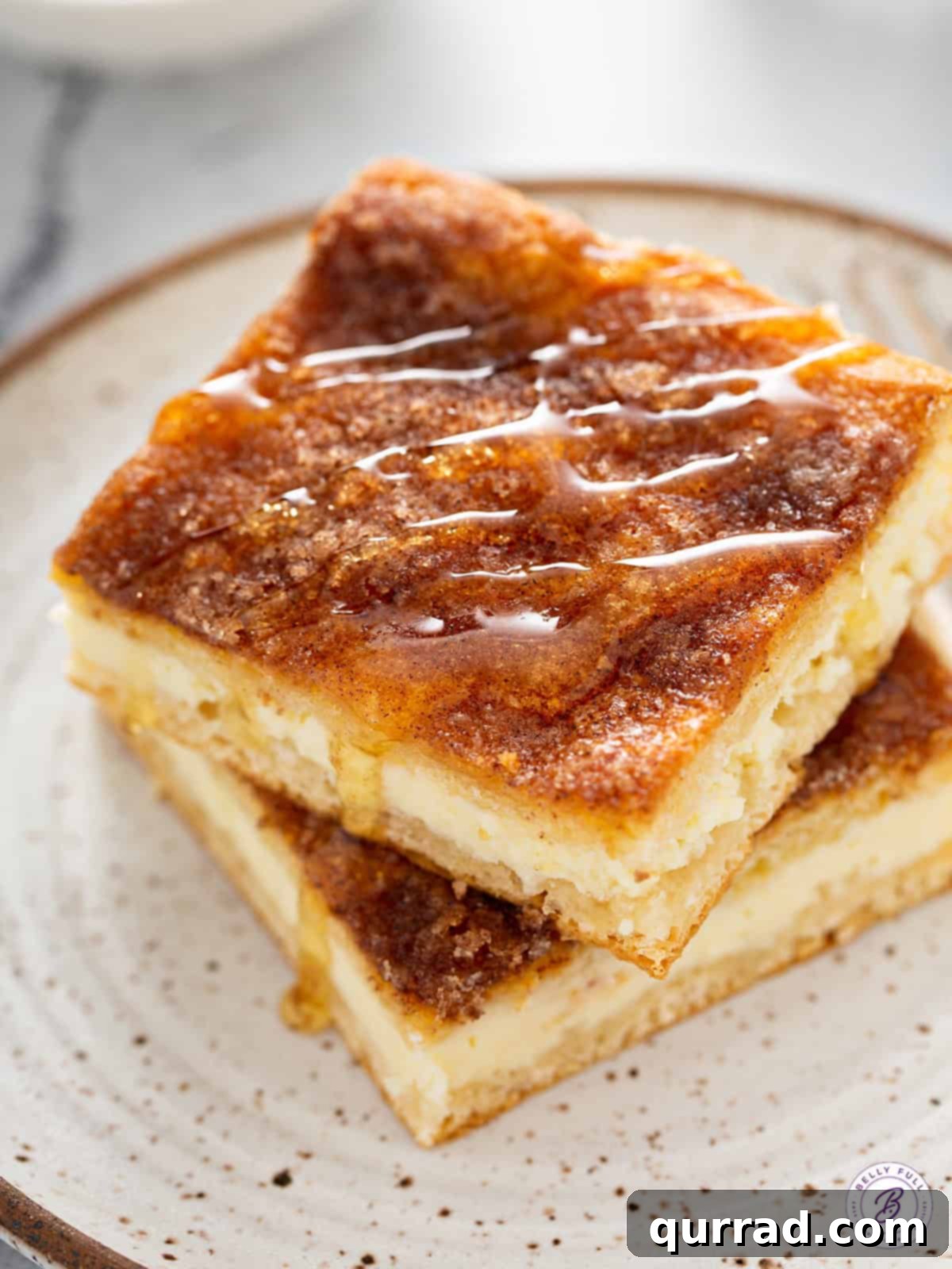 Honey Kissed Sopapilla Cheesecake 2 Golden Sopapilla Cheesecake bars with cinnamon-sugar crust and a drizzle of honey