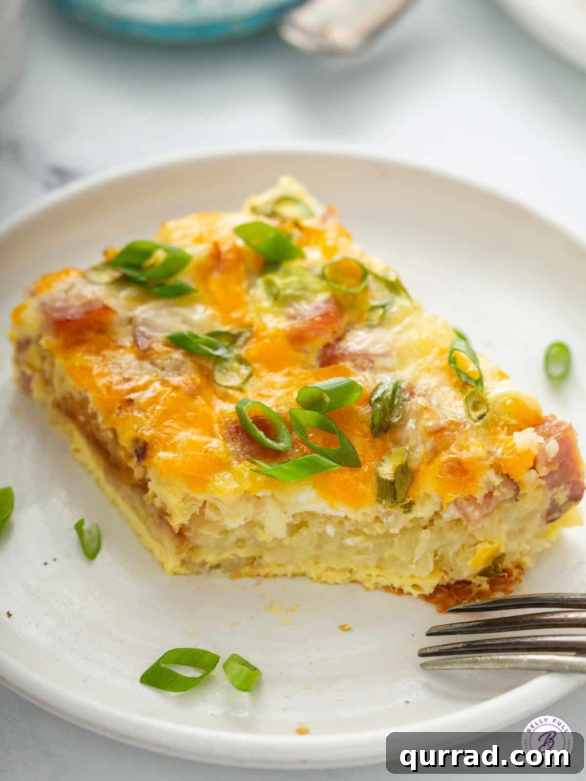 Sunrise Hash Brown Casserole 9 A close-up of a serving of hash brown egg casserole on a plate, with a fork having taken a bite, highlighting the fluffy eggs and golden hash browns.