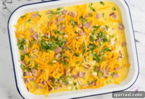 Unbaked egg custard poured over a bed of cheese and diced ham in a casserole dish, ready for the oven.