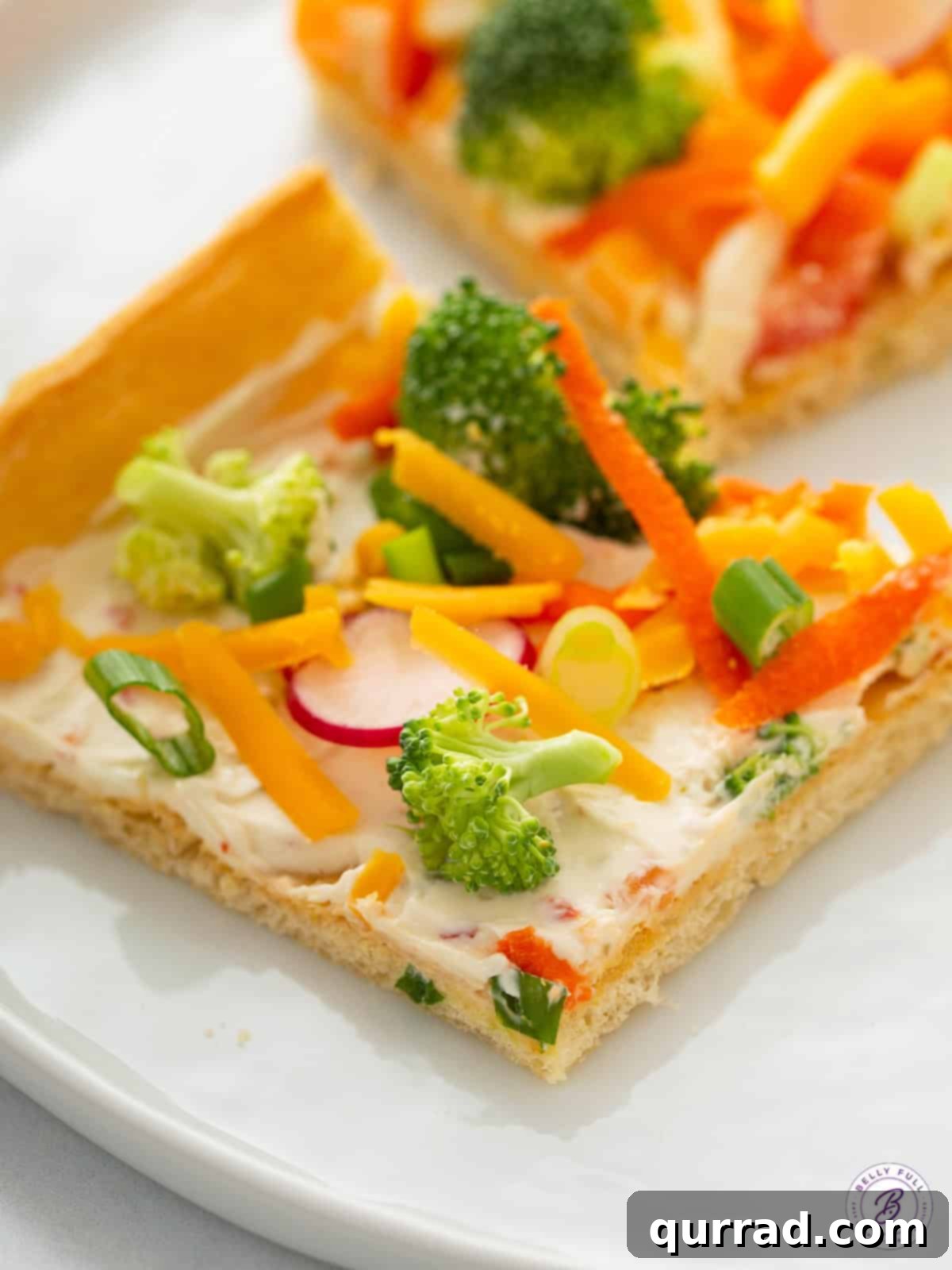 A beautifully sliced piece of Cold Veggie Pizza, showcasing the flaky, golden crescent roll crust, the creamy seasoned spread, and the vibrant array of fresh, crisp vegetable toppings. The slice is ready to be picked up and enjoyed.