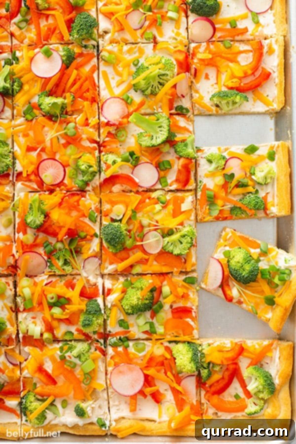 Overhead view of a baking sheet with multiple squares of Crescent Roll Veggie Pizza, neatly arranged and ready for serving to a crowd. The pizza is vibrant with fresh vegetables.