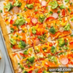 A beautifully presented overhead shot of a cold veggie pizza, with vibrant vegetables on a creamy base, meticulously cut into squares for easy serving.