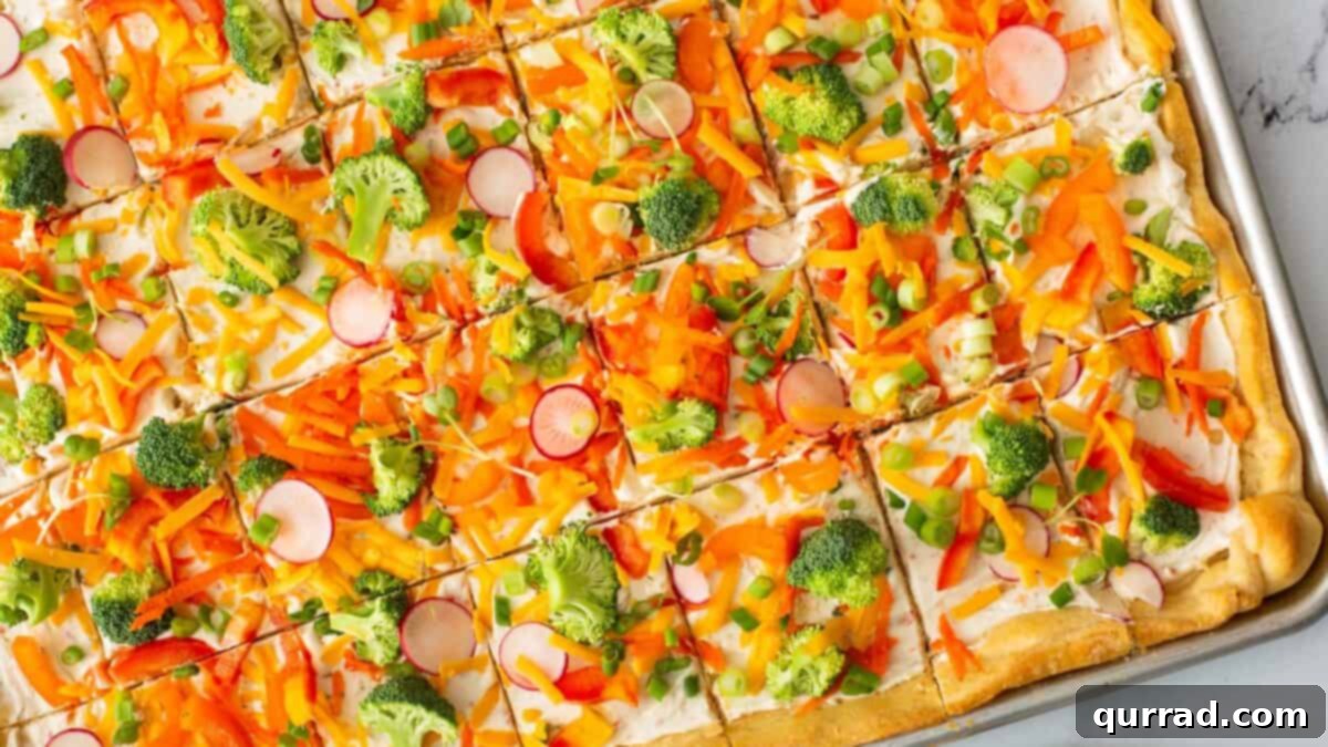 The cream cheese-covered crust now vibrantly topped with a colorful scattering of shredded sharp cheddar cheese, followed by a generous spread of finely chopped fresh broccoli, diced red and yellow bell peppers, shredded carrots, and thinly sliced green onions.