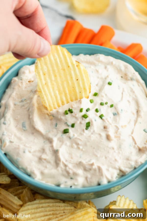 Gourmet French Onion Dip 2 A wavy potato chip being dunked into a bowl of creamy homemade French Onion Dip, highlighting its rich texture and savory appeal.