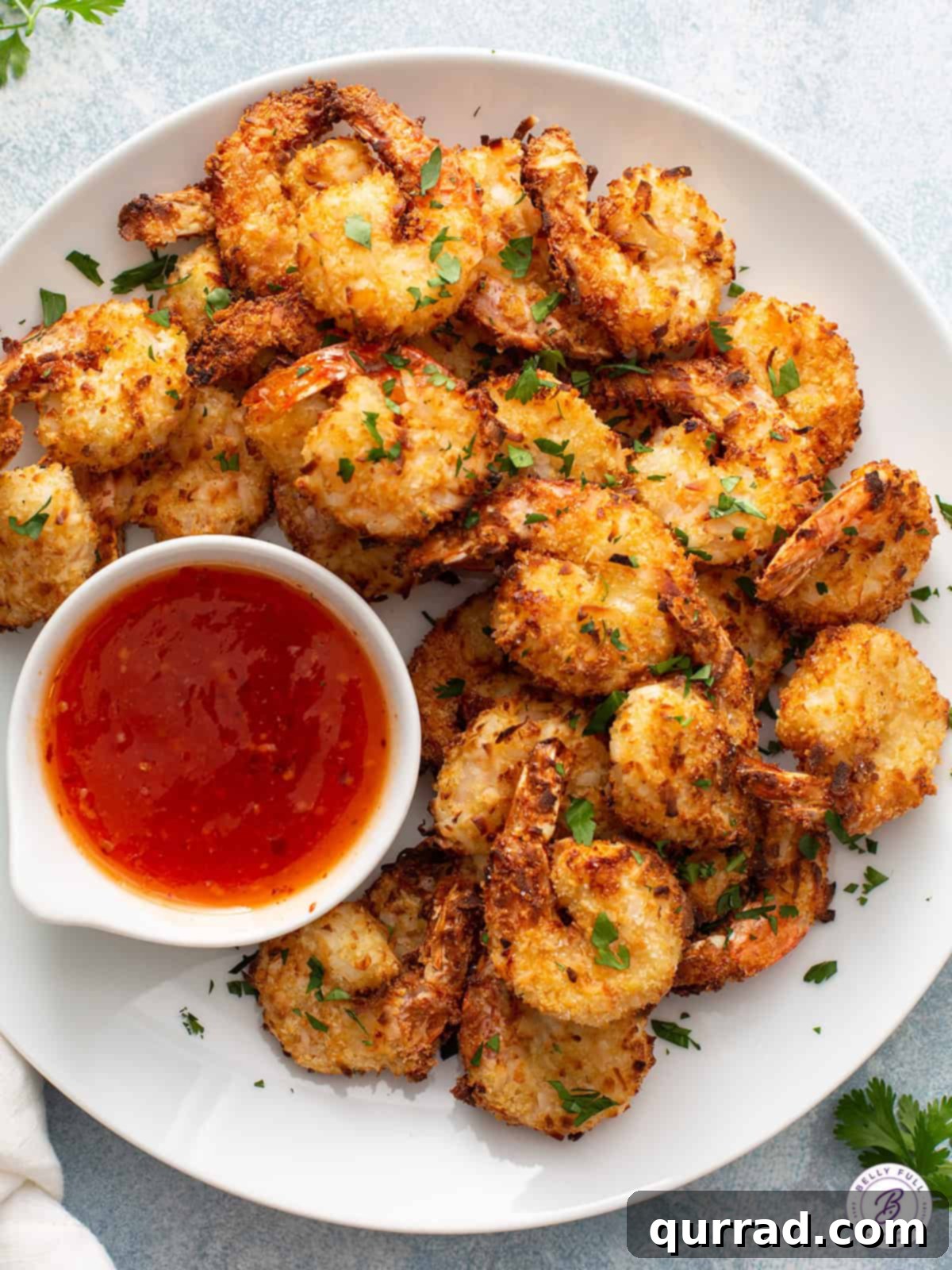 Crispy Air Fryer Coconut Shrimp 8 A serving of golden Air Fryer Coconut Shrimp garnished with fresh cilantro and a side of sweet chili dipping sauce, arranged on a rustic wooden board.