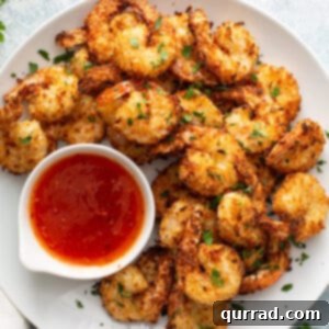 Overhead shot of golden brown Air Fryer Coconut Shrimp on a plate, with a small bowl of sweet chili dipping sauce beside them.