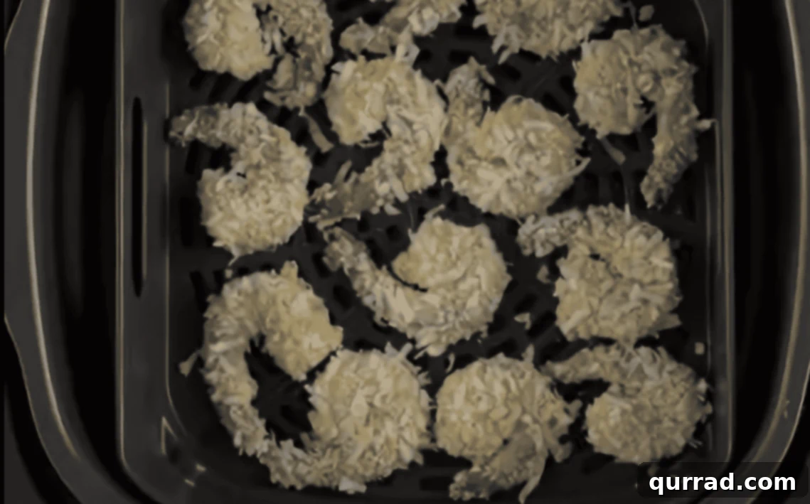 Crispy Air Fryer Coconut Shrimp 7 Several breaded coconut shrimp arranged in a single layer within an air fryer basket, ready to cook.