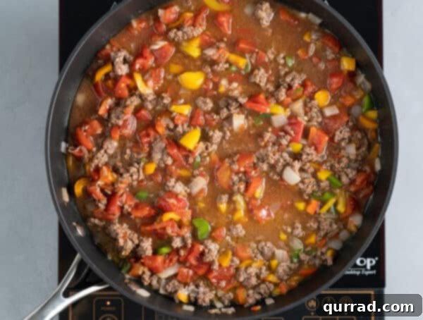 Flavor-Packed Peppers 7 Dolgulu biber harcı tencerede et suyu, domates ve pirinçle kaynıyor, zengin bir sos oluşturuyor.