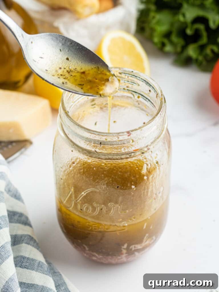 Zesty Homemade Italian Vinaigrette 3 Homemade Italian dressing dripping from a spoon back into a glass mason jar, showcasing its smooth texture.