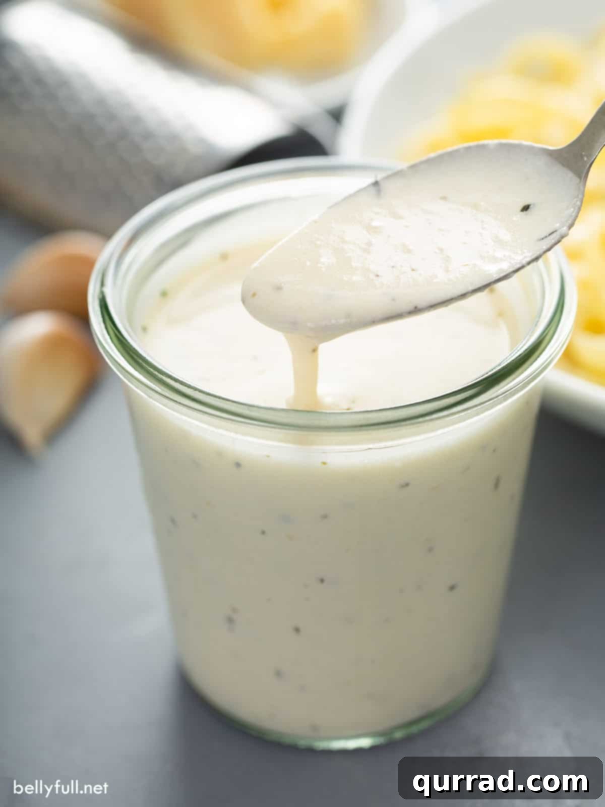 Homemade Alfredo Sauce dripping off spoon into jar, showcasing its rich and creamy texture