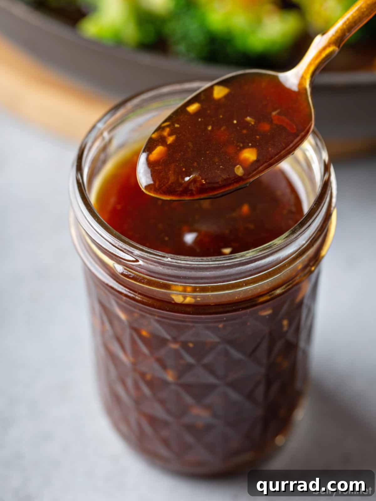 Essential Stir Fry Base 2 Homemade All-Purpose Stir Fry Sauce on a spoon, held over a glass mason jar, ready for use or storage. The sauce is rich and glossy.