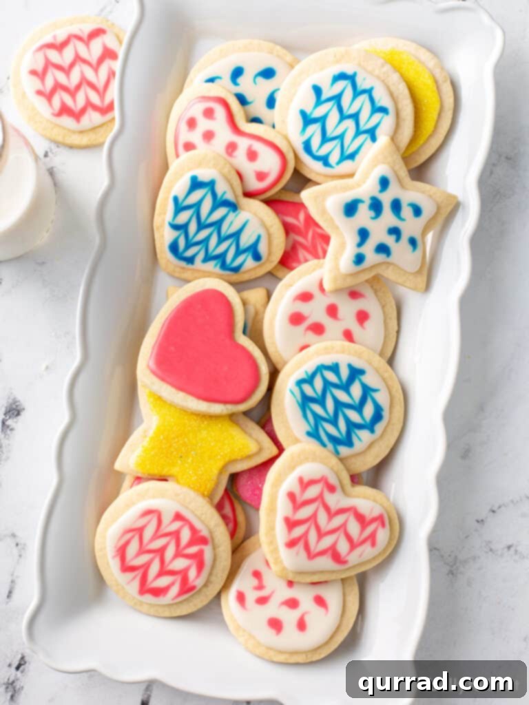 Flawless Sugar Cookie Icing 2 decorated cookies in blue, pink, and yellow sugar cookie icing, a perfect easy sugar cookie icing for beginners