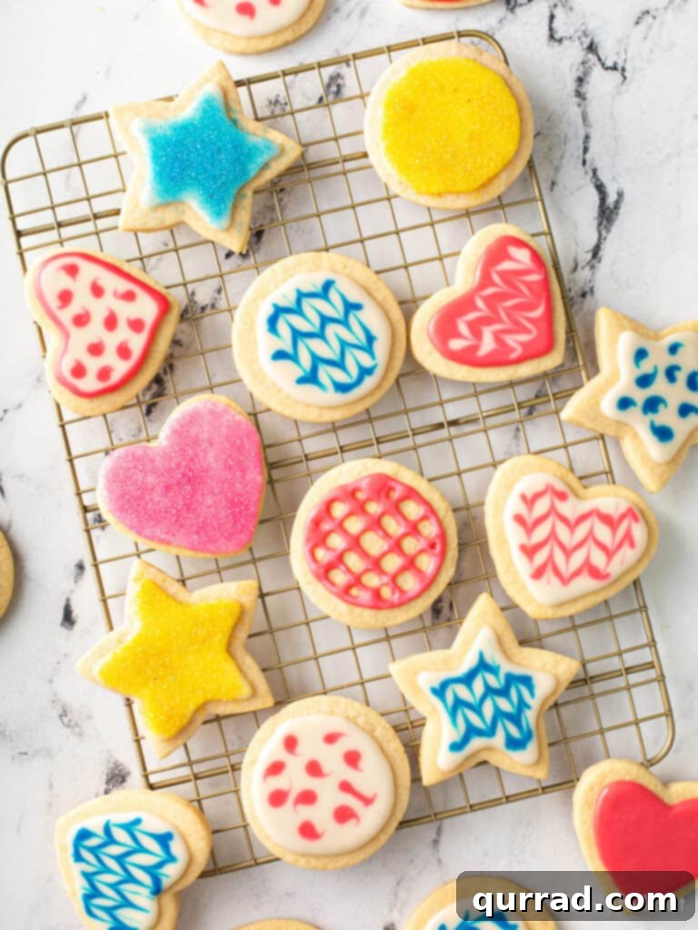Flawless Sugar Cookie Icing 3 decorated sugar cookies on wire rack with blue, pink, and yellow icing, showing the shiny, hard glaze