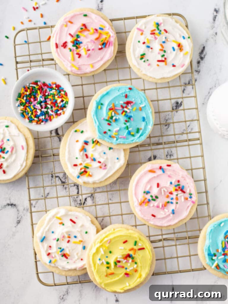 Best Sugar Cookie Frosting 3 Assortment of pastel-frosted sugar cookies with colorful sprinkles drying on a wire rack.