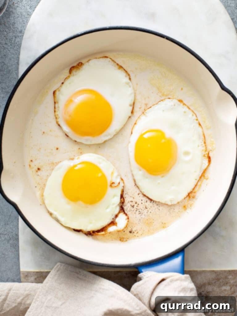 Three perfectly fried sunny side up eggs in a cast iron pan