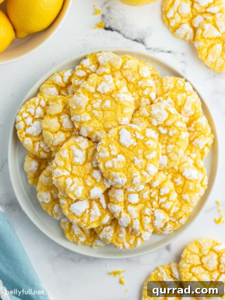 A stack of golden Lemon Crinkle Cookies dusted with powdered sugar, showcasing their signature crackled tops, on a white plate, ready to be enjoyed.