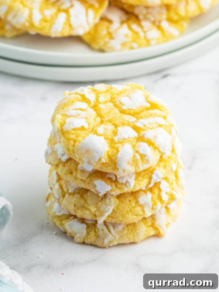 A close-up stack of four fluffy Lemon Crinkle Cookies, each perfectly dusted with powdered sugar and featuring beautiful, defined crinkles.