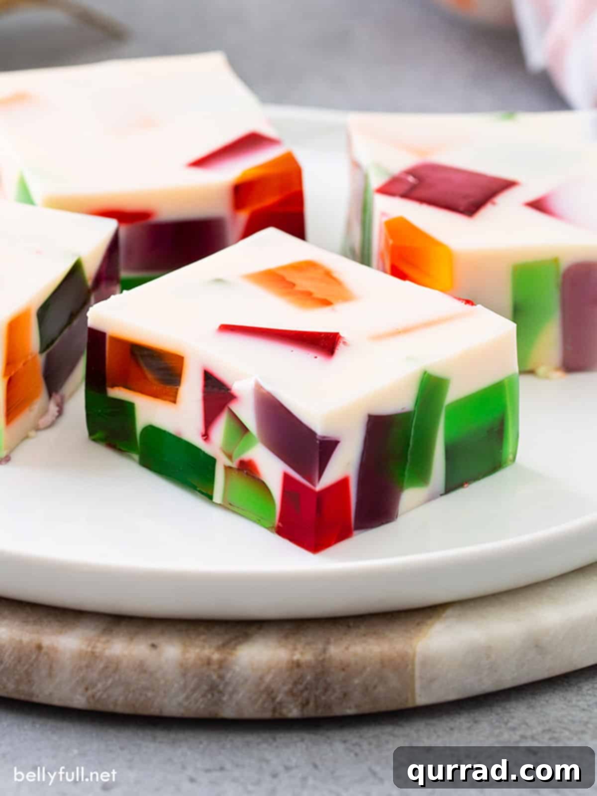 Close-up of a square piece of colorful Broken Glass Jello on a white plate, showcasing its vibrant layers and jiggly texture.