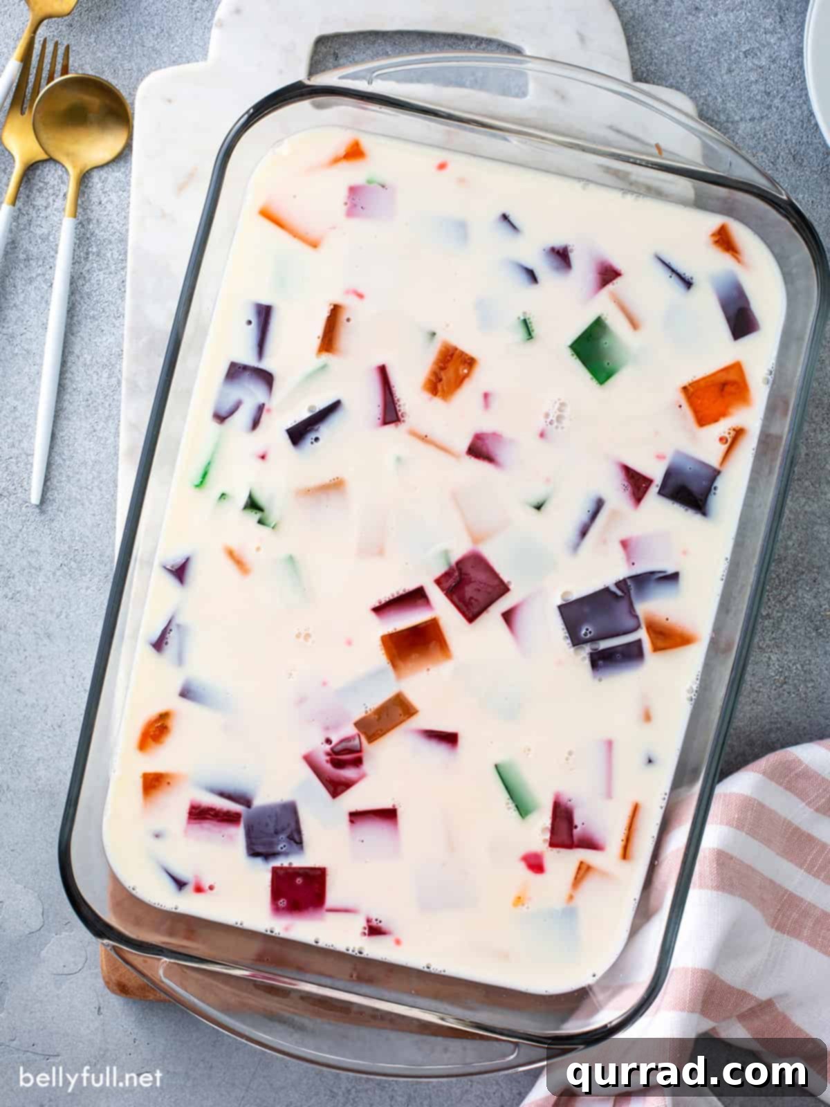 Overhead view of a rectangular glass baking dish filled with uncut Stained Glass Jello, showing the vibrant cubed Jello suspended in a creamy white base.