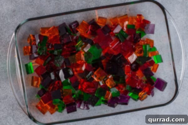 Small cubes of orange, red, green, and purple Jello gently mixed in a clear casserole dish.
