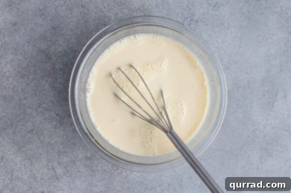 Creamy white custard mixture in a bowl with a whisk, ready to be poured.
