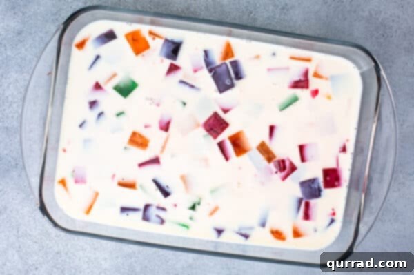 Colorful small cubes of Jello suspended in the white custard mixture in a casserole dish.