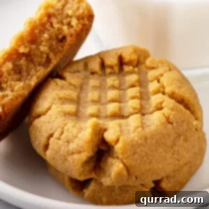 Three perfectly baked peanut butter cookies arranged on a white plate, two whole and one split in half, showcasing their chewy interior.