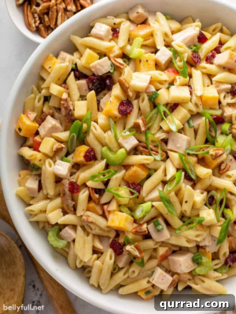 Crisp Apple Turkey Pasta Salad 2 Overhead close-up shot of a vibrant Turkey Apple Pasta Salad in a large white serving bowl, showcasing diced smoked turkey, bright apple pieces, green celery, cheese cubes, and a creamy dressing. Perfect for any gathering.