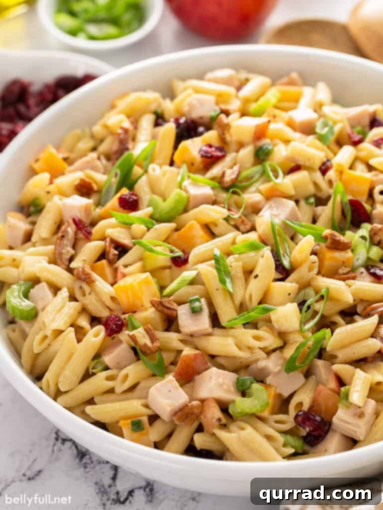 Crisp Apple Turkey Pasta Salad 3 A large white serving bowl filled with a delightful Turkey Apple Pasta Salad, featuring an appetizing mix of pasta, smoked turkey, colorful apples, and creamy dressing.