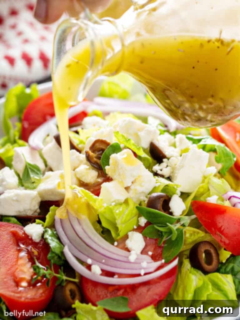 Vibrant vinaigrette dressing being poured generously over a fresh, colorful Greek salad.