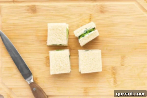 A large cucumber sandwich being precisely cut into four mini tea sandwiches.
