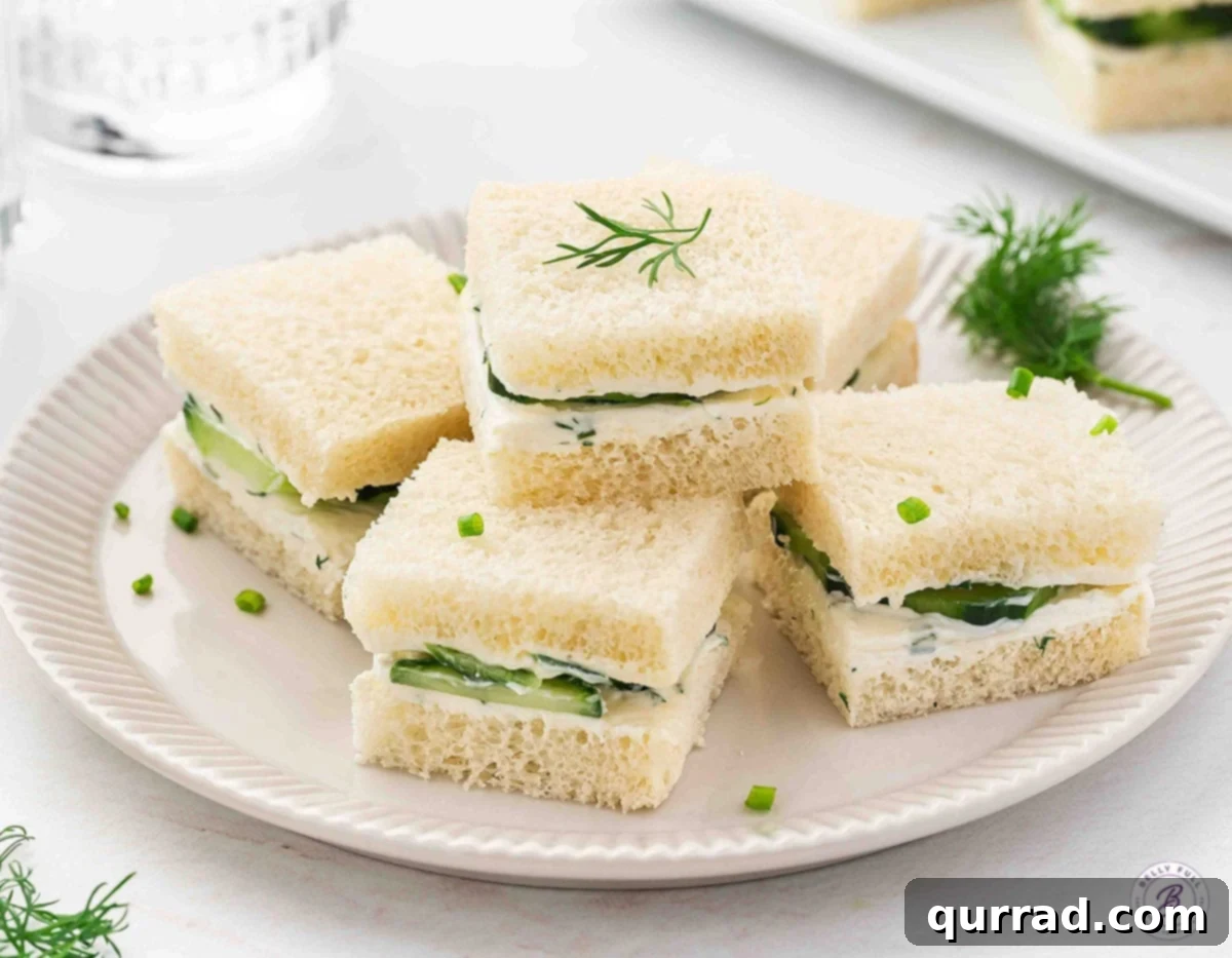 A delightful arrangement of square cucumber tea sandwiches, stacked elegantly on a pristine plate.
