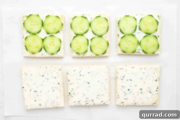 Cucumber slices layered onto bread with cream cheese spread, ready to be topped.