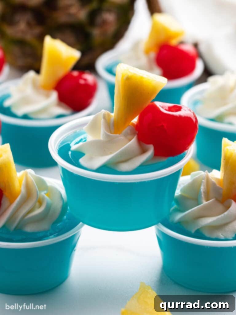 Electric Blue Hawaiian Shots 4 Three stacked Blue Hawaiian Jello Shots, each elegantly topped with whipped cream, a maraschino cherry, and a small pineapple wedge, ready to serve.