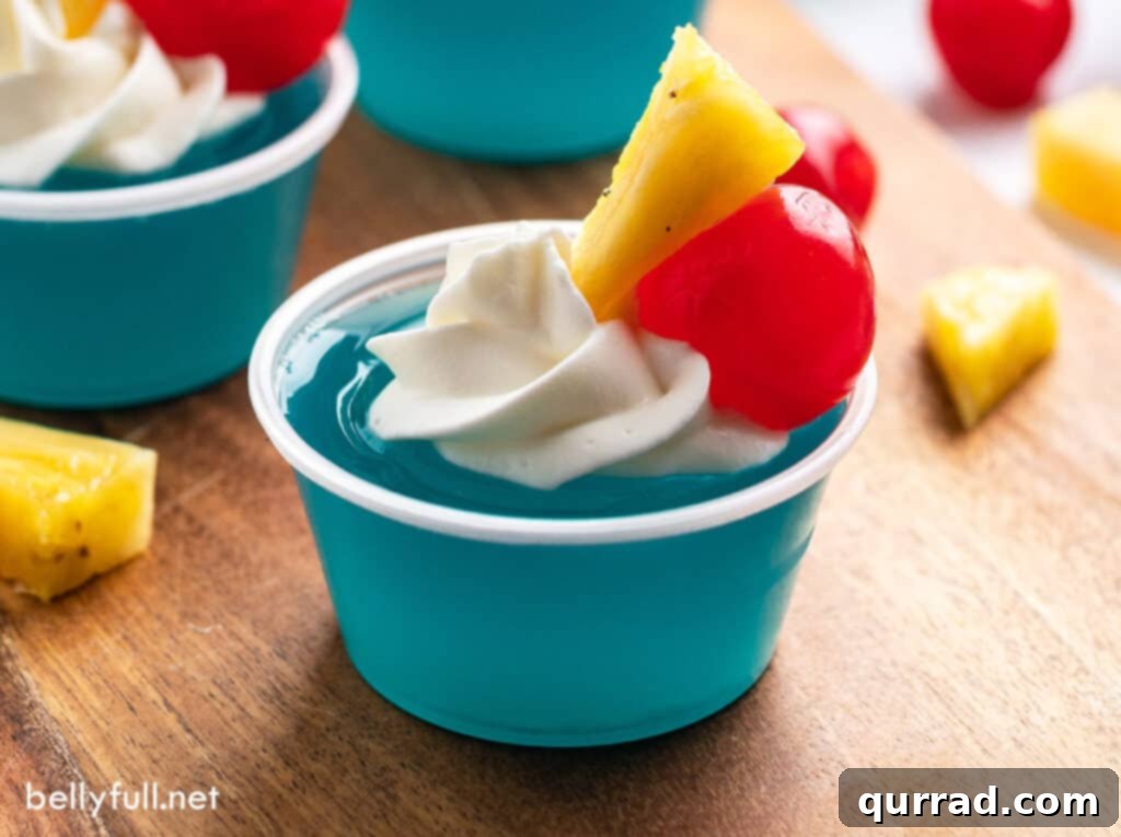Electric Blue Hawaiian Shots 5 Close-up of a single Blue Hawaiian jello cup, beautifully garnished with a pineapple wedge and a maraschino cherry, set against a blurred background.