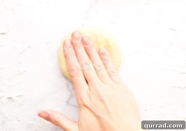 Pillowy Indian Flatbread 10 A ball of dough being gently flattened with a hand on a floured surface