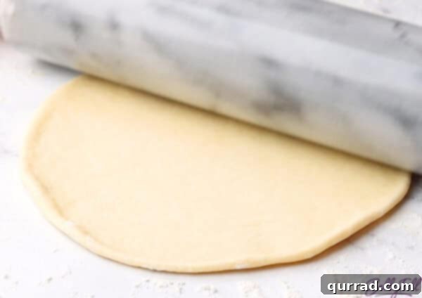 Pillowy Indian Flatbread 11 Uncooked naan dough being rolled flat with a rolling pin on a floured surface