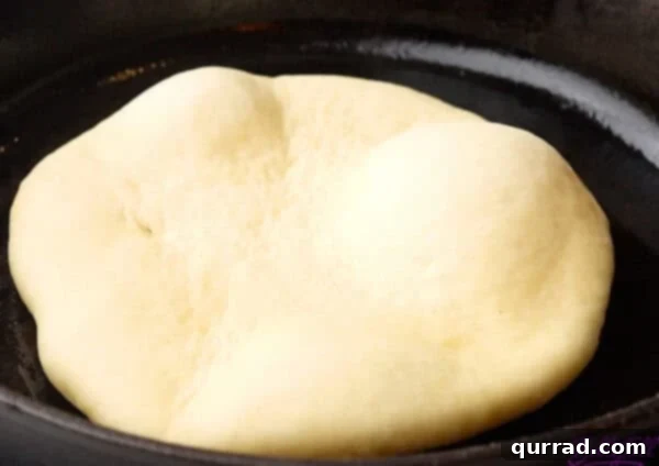 Pillowy Indian Flatbread 13 Uncooked naan dough cooking in a skillet, showing visible bubbles forming on its surface